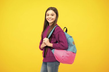 Okul üniformalı okul çantalı kız. Okul çocuğu, genç öğrenci sırt çantasını sarı izole edilmiş arka planda tutuyor.
