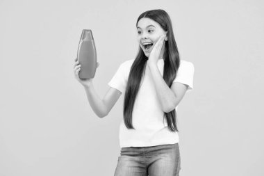 Şampuan kremi kullanan bir çocuk. Günlük kozmetik bakım. Gençlerin elinde saç ve cilt bakımı şişesi var. Güzellik sağlığı ve kozmetik ürünleri. Heyecanlı bir genç, şaşkın ve neşeli duygular içinde