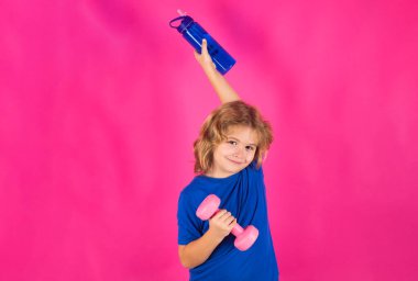 Sportif çocuklar, pembe arka planda stüdyo izole edilmiş portre. Çocuk kaslarını dambılla şişiriyor. Dambılı spor çocukları.