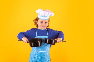 Kid chef cook with cooking pot stockpot. Kid in cooker uniform and chef hat preparing food on studio color background. Cooking, culinary and kids food concept