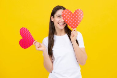 Beautiful girl holding valentines gift on yellow background. Portrait of young woman holding red paper heart