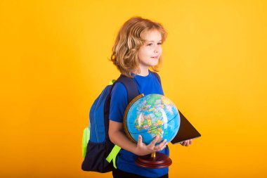Okul çocuğu dünya küresi ve tableti. İlkokulda okuyan bir okul çocuğu. Çocuk sarı izole edilmiş arka plan üzerine ders çalışıyor.