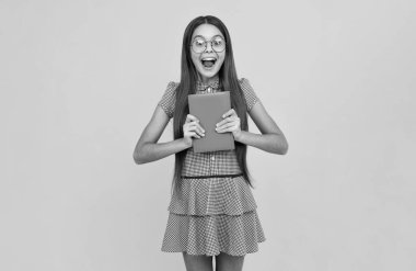 Şaşırmış genç kız. Kopya kitabı olan liseli kız izole edilmiş arka planda poz veriyor. Edebiyat dersi, ilkokul. Entelektüel çocuk okuyucusu. Heyecanlı bir ifade, neşeli ve mutlu.