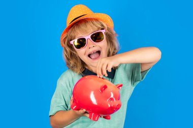 Seyahat için para biriktiriyorum. Para kutusuna para koyan küçük bir çocuğun portresi. Çocuk mavi arka planda bir kumbarada para biriktiriyor