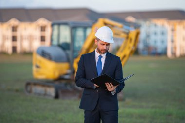 İnşaat mühendisi inşaat alanında çalışıyor. Evin arka planındaki mühendis. Modern ev inşaatında kendine güvenen mühendis. İspanyol inşaat mühendisi miğferinde