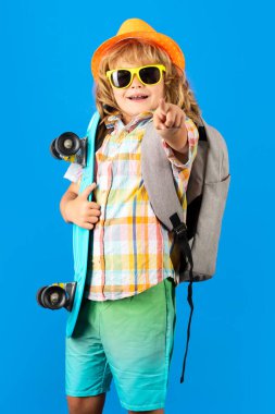 Mavi arka planda uzun tahta tutan çocuk. Pennyboard 'u olan çocuk. Moda şapkalı ve güneş gözlüklü neşeli küçük çocuğun stüdyo fotoğrafı.