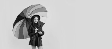 Gökkuşağı şemsiyesi altında şapkalı ve deri elbiseli mutlu genç kız, sonbahar yağmuru. Sonbahar şemsiyeli çocuk, yağmurlu hava, yatay poster, fotokopi alanı olan afiş
