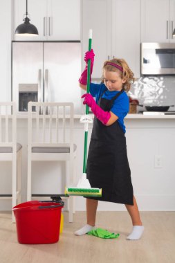 Portrait of child cleaning, concept growth, development, family relationships. Housekeeping and home cleaning concept. Child use duster and gloves for cleaning. Home kitchen background