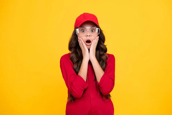 身穿红色工作服 戴帽子和戴防护眼镜的少年劳动者 工作室拍摄的肖像孤立在黄色背景 令人惊讶的少女 — 图库照片