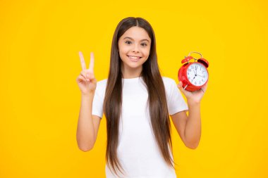 Sarı arka planda saati olan çocuk öğrenci kız. Çocuk okula geri döndü. Eğitim ve zaman kavramı. Mutlu ergen portresi. Gülümseyen kız