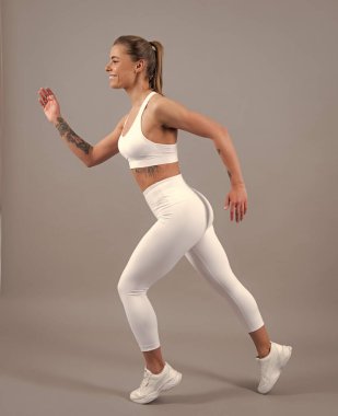 Genç sporcu kadın koşucu koşmadan önce bacaklarını esnetiyor. Gri arka planda sportif kadın koşucu. Dinamik hareket. Spor ve sağlıklı yaşam tarzı