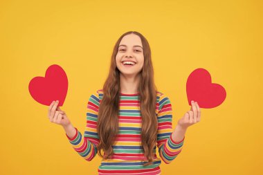 Neşeli romantik genç kız sarı arka planda izole edilmiş sevgililer günü için aşkın kırmızı kalp sembolünü taşıyor.