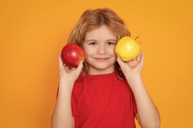 Çocuklar için vitamin ve sağlıklı meyveler. Stüdyoda elmalı kırmızı tişörtlü çocuk. Stüdyo portresi sarı arka planda elma tutan şirin bir çocuk.