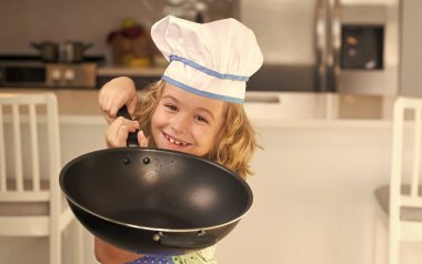 Komik çocuk mutfak masasında durur, yemek pişirir, fırın yapar, evde yemek pişirir.