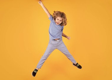Full body of little child jump wear casual t-shirt and jeans isolated on yellow background