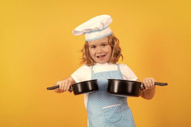 Kid chef cook with cooking pot stockpot. Kid in cooker uniform and chef hat preparing food on studio color background. Cooking, culinary and kids food concept