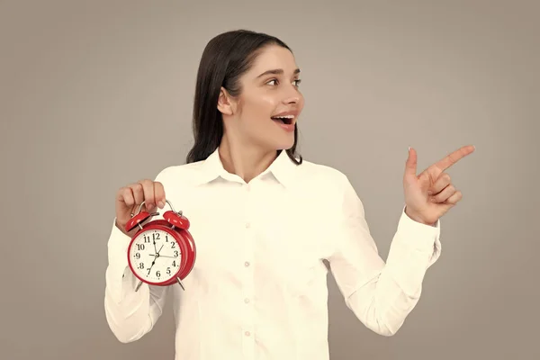 Beautifu women with clock. Portrait of young attractive shocked amazed surprised girl hold clock isolated on gray color background