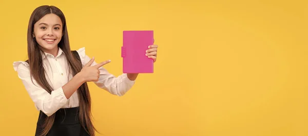 stock image happy teen girl in school uniform pointing finger on book, advertising. Portrait of schoolgirl student, studio banner header. School child face, copyspace