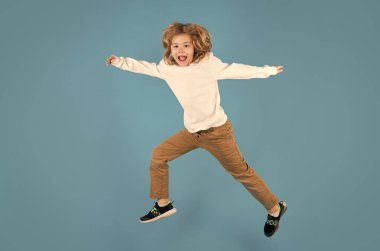 Full length body size of carefree child jump isolated over blue background. Kid boy jumping and raising hand up