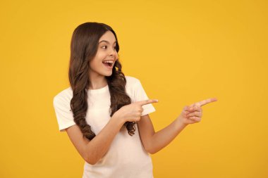 Close-up portrait of her she nice cute attractive cheerful amazed girl pointing aside on copy space isolated on yellow background. Amazed teenager. Excited teen girl