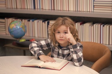 Eğitim, bilgi ve kitapçı konsepti. Çocuk kütüphanede kırmızı bir kitap okuyor. Okul kütüphanesindeki küçük öğrenci.