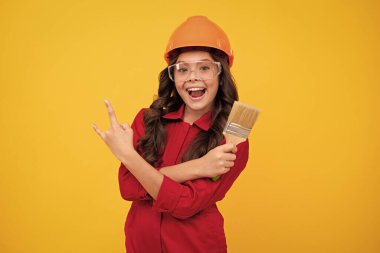 Miğferli çocuk müteahhidi. Fırça aletli ya da boya silindirli genç kız ressam. Sarı arka planda izole edilmiş tamir işindeki çocuk. Çocuk yenileme konsepti. Mutlu genç kız