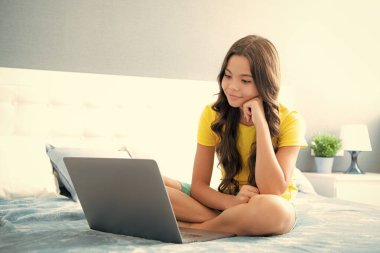 Genç kız evdeki yatak odasındaki dizüstü bilgisayarda internette geziniyor. Mutlu genç kız, pozitif ve gülümseyen duygular
