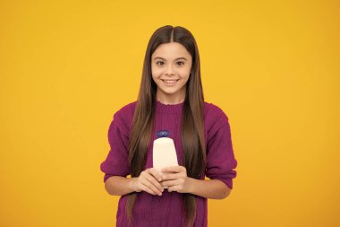 Genç kız, sarı arka planda şişe şampuanı ya da duş jeli gösteriyor. Saç kozmetik ürünü. Şişeyi hazırla.