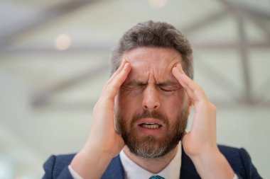 Yorgun adamın korkunç bir baş ağrısı var. Bitkin, sağlıksız hisseden, baş ağrısı hastalığına üzülen bir adam. Stresli orta yaşlı adamın başı ağrıyor. Migren ve baş ağrısı konsepti