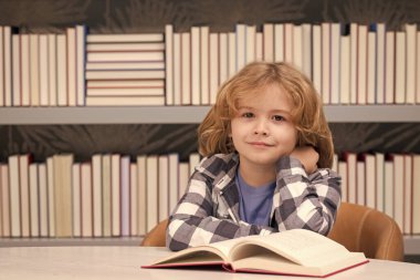 School child studying in school library. Portrait of child reading in library on background with books