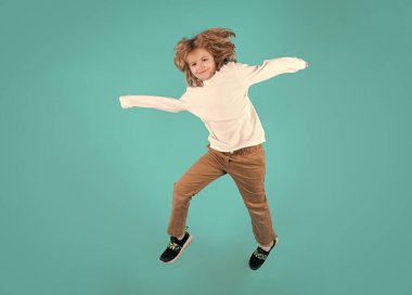 Havaya uçan komik çocuk. Enerjik çocuk atlıyor ve el kaldırıyor. Yükseklerden atlayan çocuğun boy boy boy fotoğrafı mavi arka planda hızla koşarken.