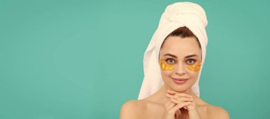 Göz bantları, göz altı bantları. Pozitif genç kadının yüzünde havluyla kolajen altın göz bantları var. Güzel kadın, izole edilmiş yüz portresi, taklit alanı olan pankart.