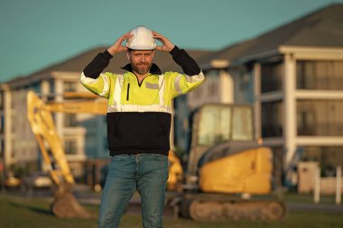 Portrait of worker man small business owner. Construction worker with hardhat helmet on construction site. Construction engineer worker in builder uniform with excavation truck digging. Worker