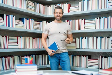 Kütüphanede kitabı olan bir öğretmenin portresi. Üniversite kütüphanesinde yakışıklı bir öğretmen. Öğretmenler Günü. Öğretmen ders veriyor. Kütüphanede öğretmen. Kitaplıktaki üniversite kütüphanesinde özel öğretmen.