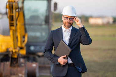 Takım elbiseli ve kasklı bir Buider. İnşaat yatırımcısı. İnşaat alanının önündeki yatırımcı. Başarılı bir yatırımcı. İnşaatta takım elbiseli yakışıklı ve kasklı bir adam.