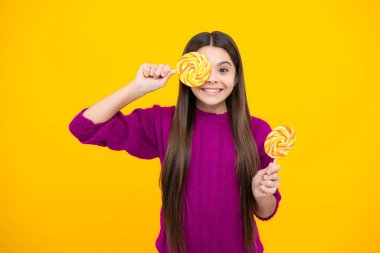 Teen girl hold lollipop caramel on yellow background, candy shop. Teenager with sweets suckers