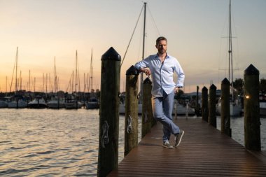 40 'lı yılların adamı yatın yanında. Dışarıdaki mankenin portresi. Moda erkeği yatların yanında poz veriyor. Şehir tarzında bir moda adamı. Yat kulübündeki yakışıklı İspanyol adam. Lüks yatın yanındaki körfezdeki adam.