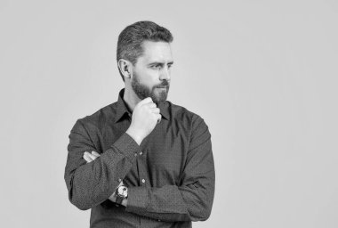 Şık sakallı, tıraşsız bir adam. Günlük tarz gömlekle ciddi görünüyor. Gri arka plan, berberlik, fotokopi alanı..