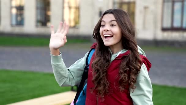 在公园里 学龄少女慢动作地挥手致意 在户外上学的少女 外面的女学生 带背包的女学生 — 图库视频影像