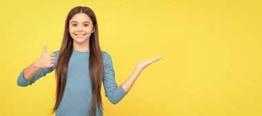 Sarı arka planda fotokopi alanı ve reklamı olan bir ürün sunan mutlu çocuk. Çocuk yüzü, yatay poster, izole edilmiş genç kız portresi, fotokopi alanı olan pankart