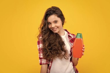 Teen child girl with shampoo bottle or shower gel isolated on yellow background. Kids hair cosmetic product. Happy teenager, positive and smiling emotions of teen girl