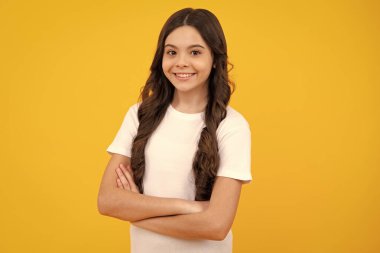 Genç kız sarı arka planda izole bir şekilde kollarını kavuşturmuş. Çocuk portresi ve fotokopi alanı. Mutlu ergen, pozitif ve gülümseyen genç kız duyguları
