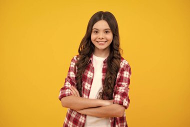 Mutlu ergen, pozitif ve gülümseyen genç kız duyguları. Kollarını kavuşturmuş genç bir kız, kameraya bakıyor, sarı stüdyo arka planında izole edilmiş.