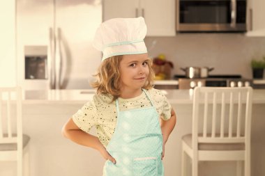 Portrait of funny child chef in kitchen. Kid chef cook is learning how to make a cake in the home kitchen. Child making tasty delicious