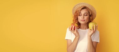 Yaz kızı elmayı tutuyor. Hasır şapkalı kadın sağlıklı yemek yiyor. Gençlik sağlığı. Doğal organik taze elma. Güzel kadın, izole edilmiş yüz portresi, taklit alanı olan pankart.