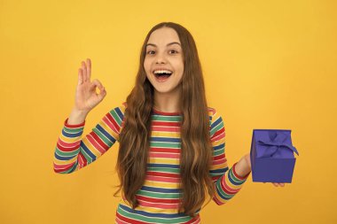 Teenage kid with present box. Teen girl giving birthday gift. Present, greeting and gifting concept. Excited face, cheerful emotions of teenager child girl