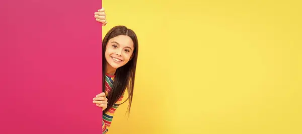 快乐的少女在粉红色的纸片后面 空空荡荡的地方复制空间 做广告 儿童脸 横向海报 少女孤家寡人肖像 横幅与复制空间 免版税图库图片