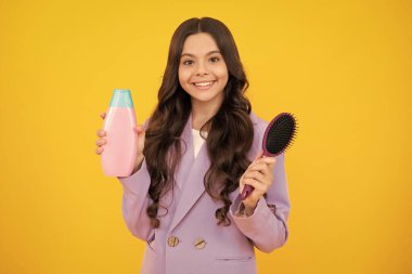 Teenager child girl showing bottle shampoo conditioners or shower gel isolated on yellow background. Hair cosmetic product. Mock up bottle. Happy face, positive and smiling emotions of teenager girl