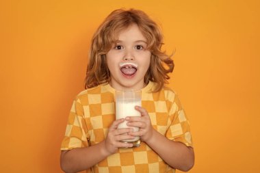 Little child drinking milk. Kid with glass of milk on yellow isolated background