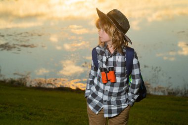 Dürbünle oynayan mutlu çocuk. Keşif ve macera. Sırt çantalı çocuk doğayı ve çevreyi keşfediyor. Çocuklar için açık hava aktivitesi. Turistler için yaz yolculuğu